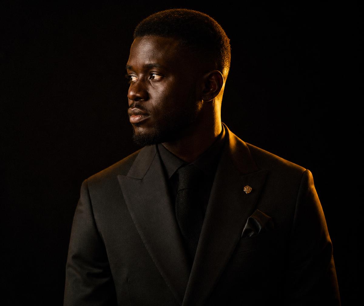 Portrait of a Black man in a tailored suit under warm gold light